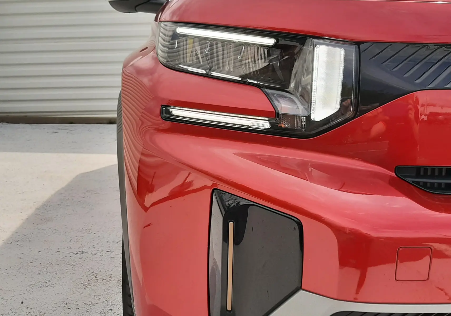 Gros plan sur l'avant gauche du Citroën C3 Aircross rouge Elixir avec toit noir, mettant en valeur son phare LED et sa calandre distinctive.