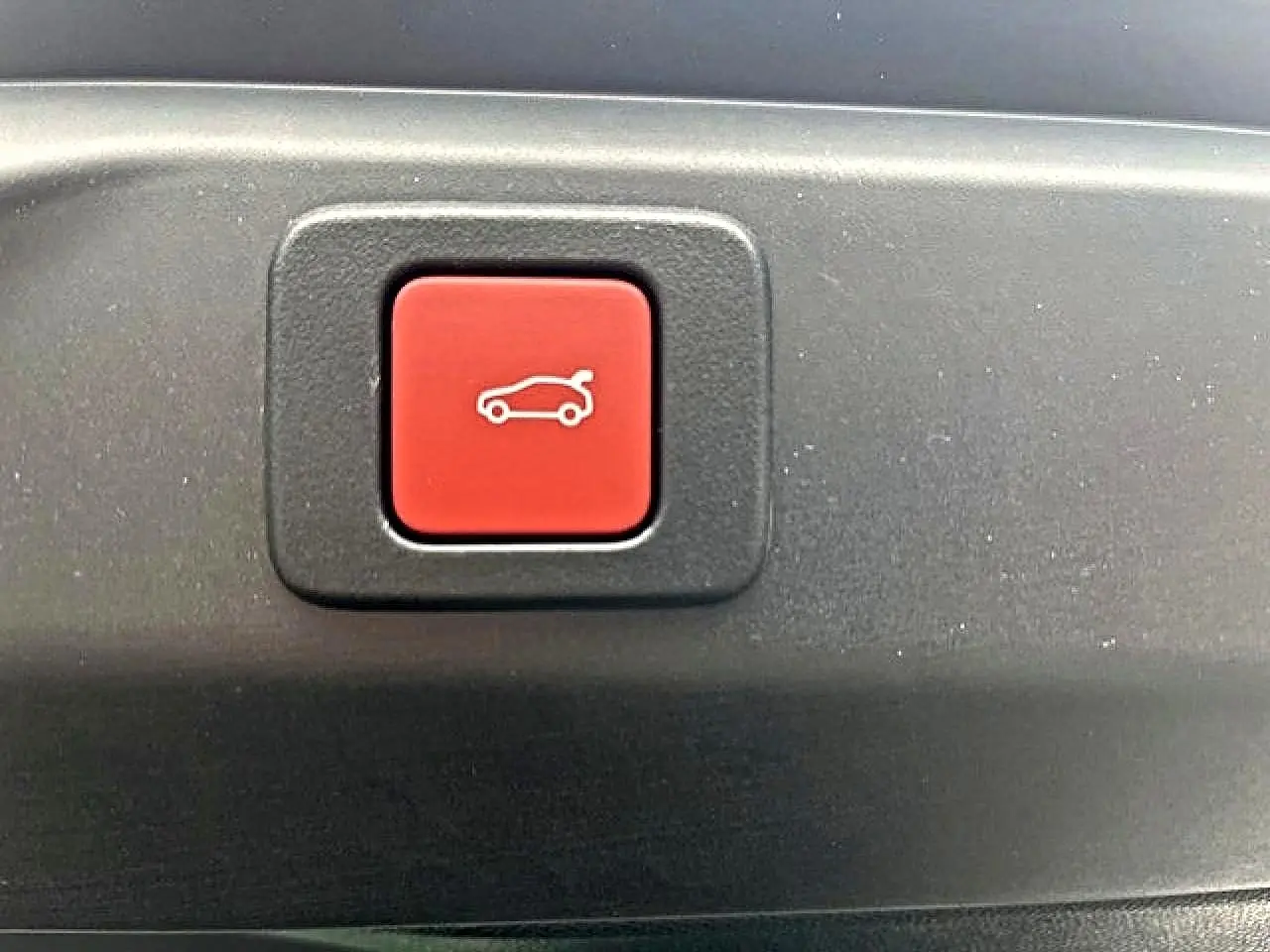 Bouton rouge d'ouverture électrique du coffre sur un Peugeot 3008 gris titane, vue en gros plan.