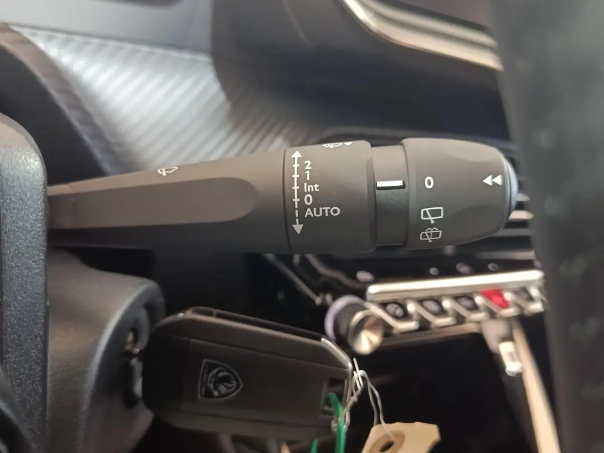 Gros plan sur la commande d’essuie-glace et clé de contact dans l’habitacle noir d’une Peugeot 208 électrique gris clair.