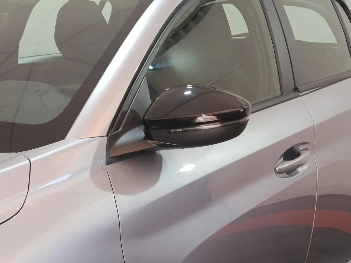 Vue rapprochée du côté gauche d'une Peugeot 208 électrique gris clair avec rétroviseur noir brillant.