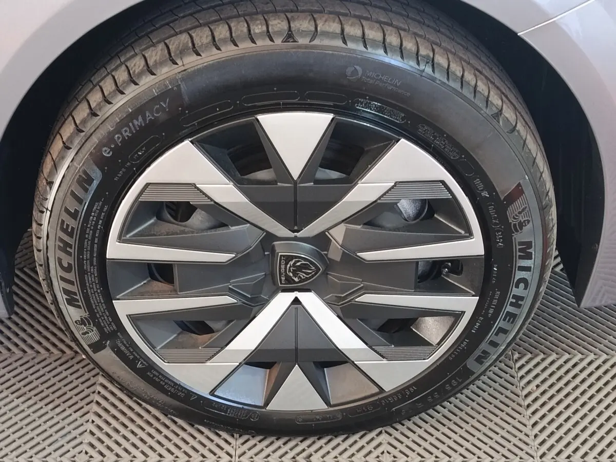 Gros plan sur la roue avant droite gris clair du Peugeot 208 électrique 2024 avec jante au design géométrique noir et argent.