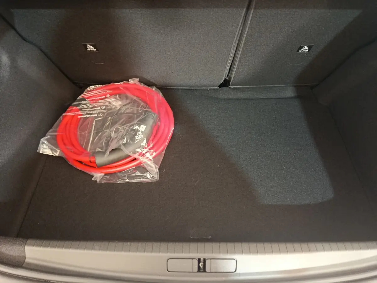 Coffre ouvert de Peugeot 208 électrique gris clair vu de dessus, avec câble de charge rouge emballé posé à gauche.