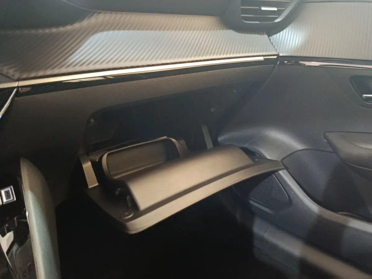 Intérieur de la Peugeot 208 électrique 2024, vue sur la boîte à gants ouverte côté passager avec finition noire et détails carbone.