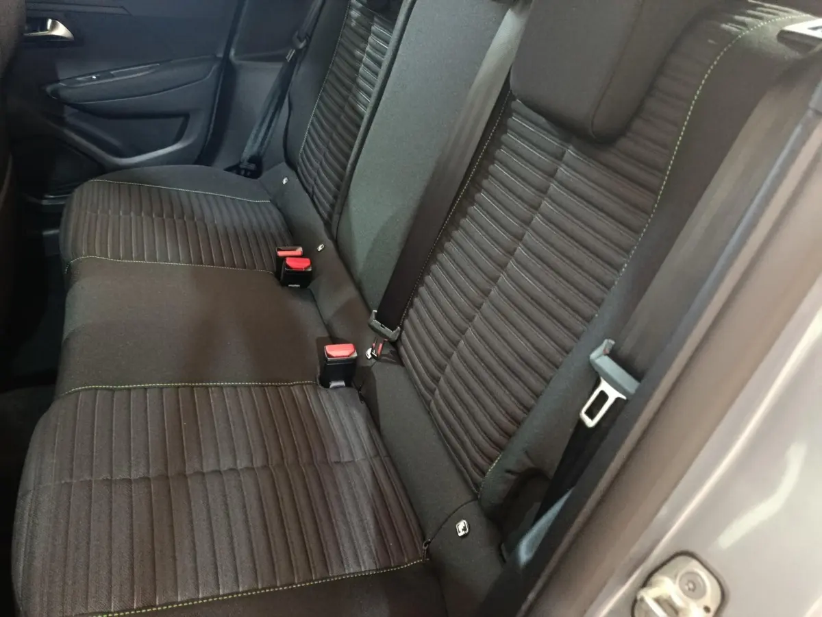 Vue latérale des sièges arrière noirs avec surpiqûres vertes d'une Peugeot 208 électrique gris clair 2024.