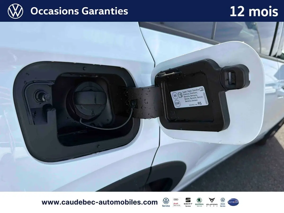 Gros plan sur la trappe à carburant ouverte côté gauche d’un Volkswagen T-Roc blanc, avec bouchon essence visible.