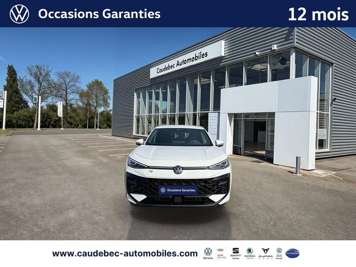 Vue avant d'un Volkswagen T-Roc blanc garé devant un bâtiment moderne avec logo VW lumineux sur la calandre.
