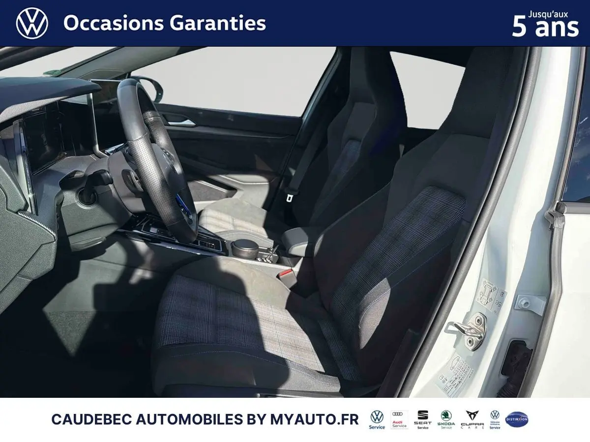 Vue intérieure côté conducteur d'une Volkswagen Golf 1.5 eHybrid blanche, sièges sport à motifs et volant multifonction cuir.