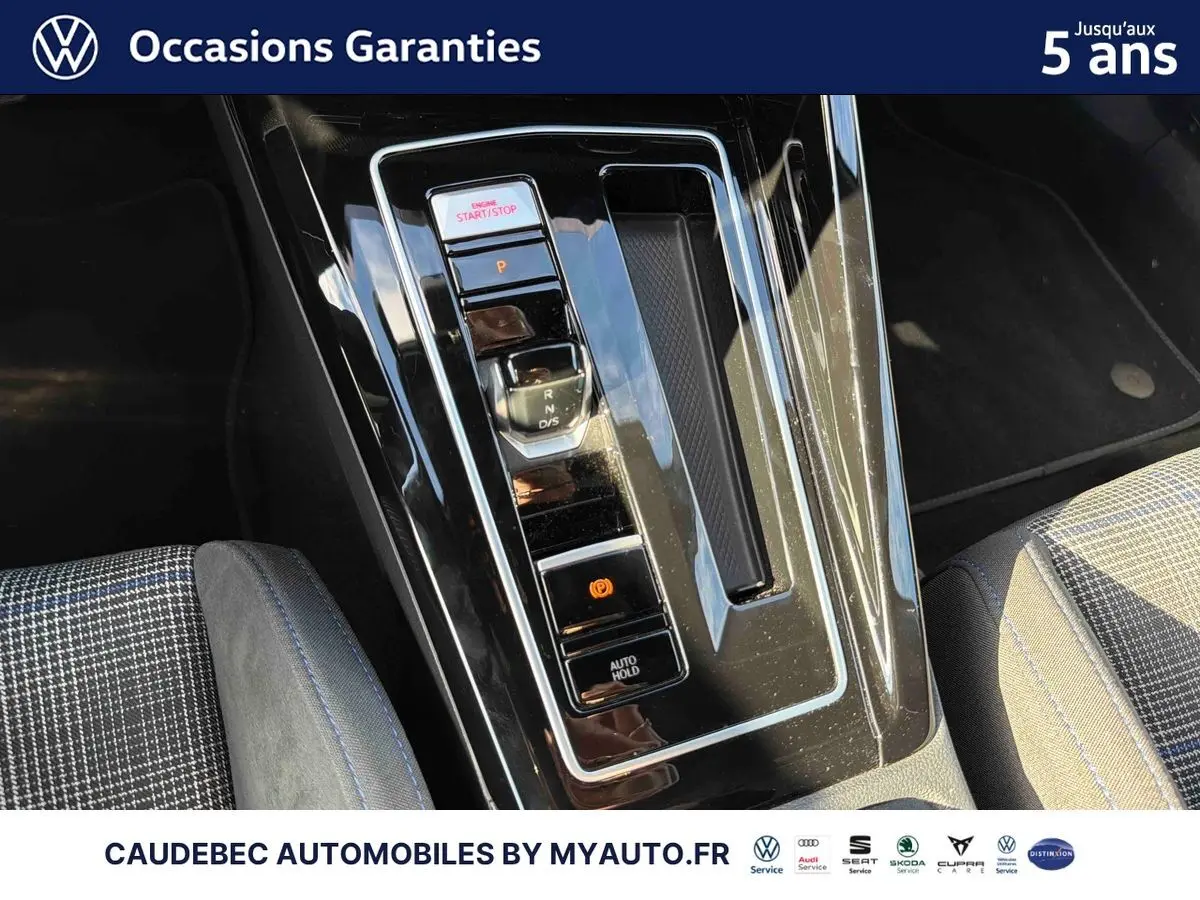 Vue rapprochée de la console centrale noire brillante de la Volkswagen Golf 1.5 eHybrid 2026 avec levier de vitesses et boutons lumineux.