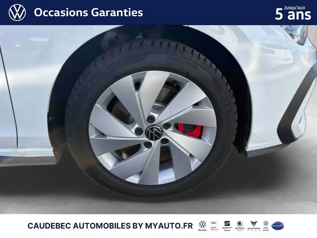 Gros plan sur la roue avant gauche d'une Volkswagen Golf blanche avec étrier de frein rouge visible.