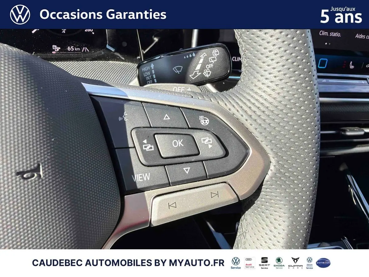 Gros plan sur les commandes multifonctions du volant en cuir perforé gris clair d'une Volkswagen Golf blanche.
