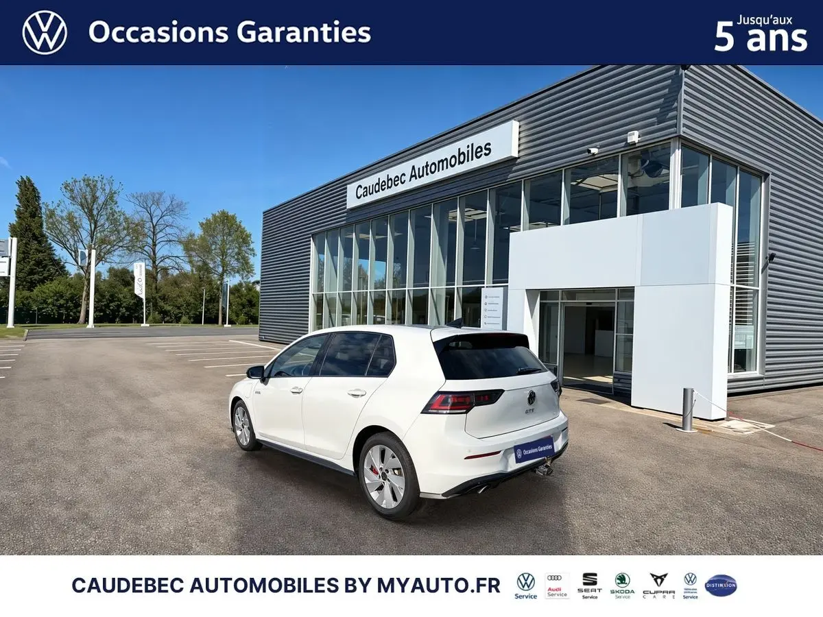Vue 3/4 arrière droite d'une Volkswagen Golf 1.5 eHybrid blanche, avec attelage escamotable et vitres surteintées.