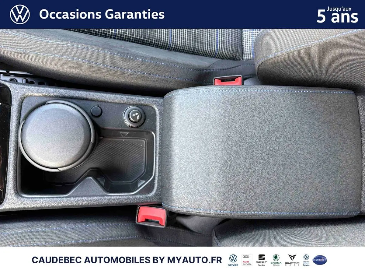 Vue plongeante sur la console centrale noire avec accoudoir et porte-gobelet de la Volkswagen Golf 1.5 eHybrid blanche.