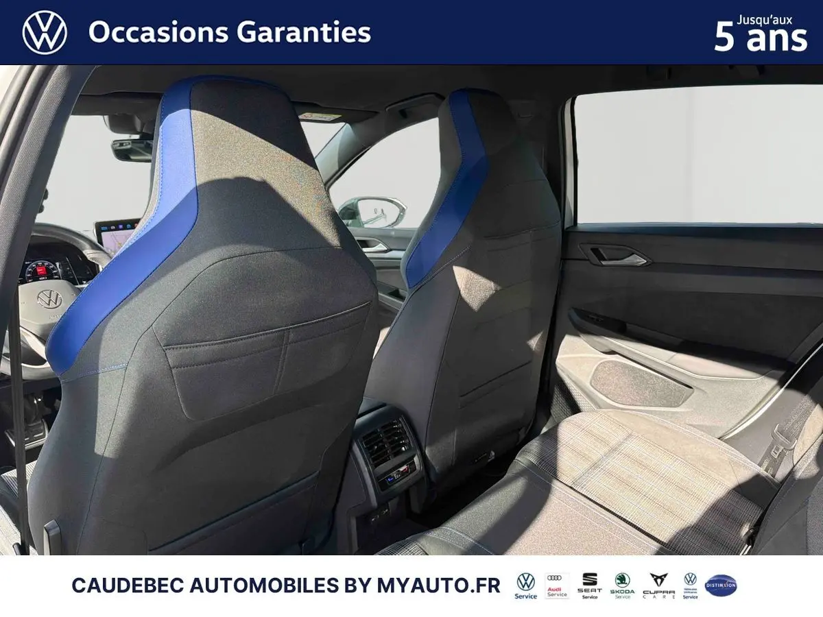 Vue intérieure arrière montrant les sièges avant noirs avec surpiqûres bleues et la banquette arrière grise à motifs de la Volkswagen Golf blanche.