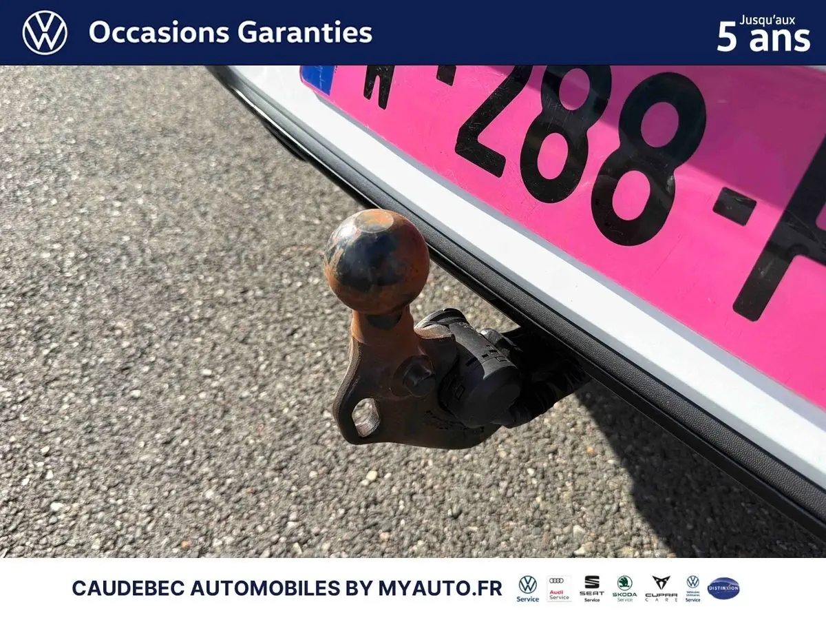 Gros plan sur l'attelage escamotable électrique à l'arrière d'une Volkswagen Golf blanche, avec plaque d'immatriculation rose.