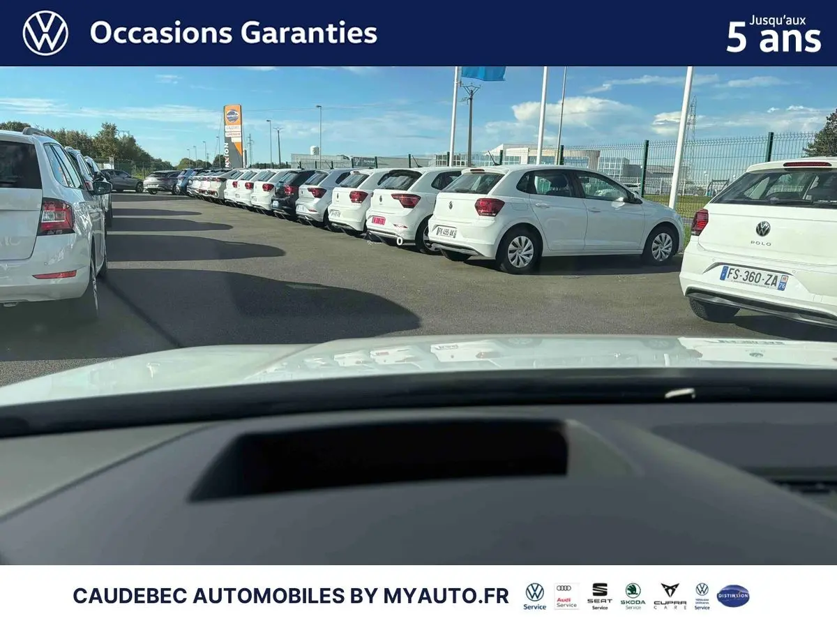 Vue depuis l'intérieur vers l'avant d'une Volkswagen Golf blanche stationnée dans un parking extérieur.