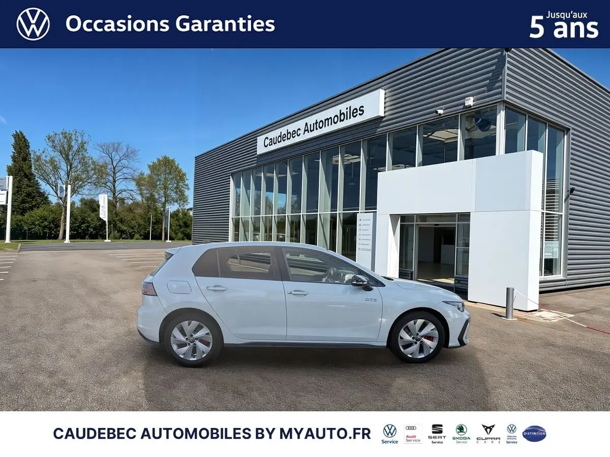 Vue latérale droite d'une Volkswagen Golf 1.5 eHybrid blanche garée devant un bâtiment commercial moderne.