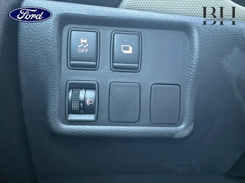 Panneau de commandes noir côté conducteur de Nissan Micra gris acier, avec boutons de contrôle de stabilité et réglage des phares.