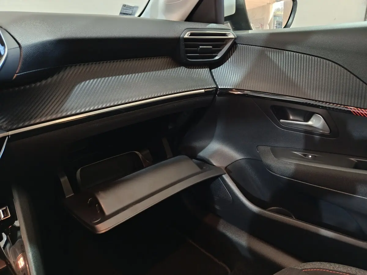 Vue intérieure côté passager du tableau de bord et boîte à gants ouverte d'une Peugeot 208 électrique blanche de 2020.