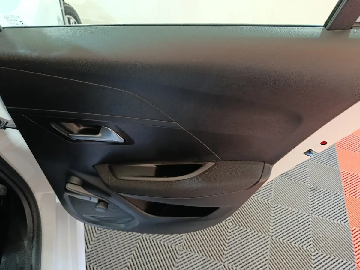 Vue intérieure de la porte arrière gauche noire d'une Peugeot 208 électrique blanche, avec poignée et commande de vitre manuelle.