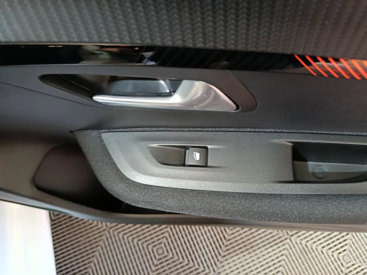 Gros plan sur la poignée intérieure et le bouton de lève-vitre côté gauche d’une Peugeot 208 électrique blanche.