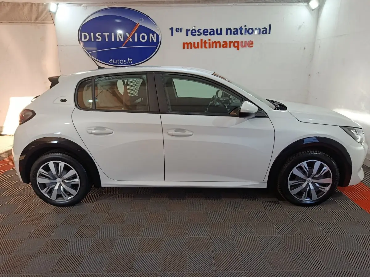 Vue de profil côté gauche d'une Peugeot 208 électrique Active Business blanche, avec jantes stylisées et logo "e" arrière.