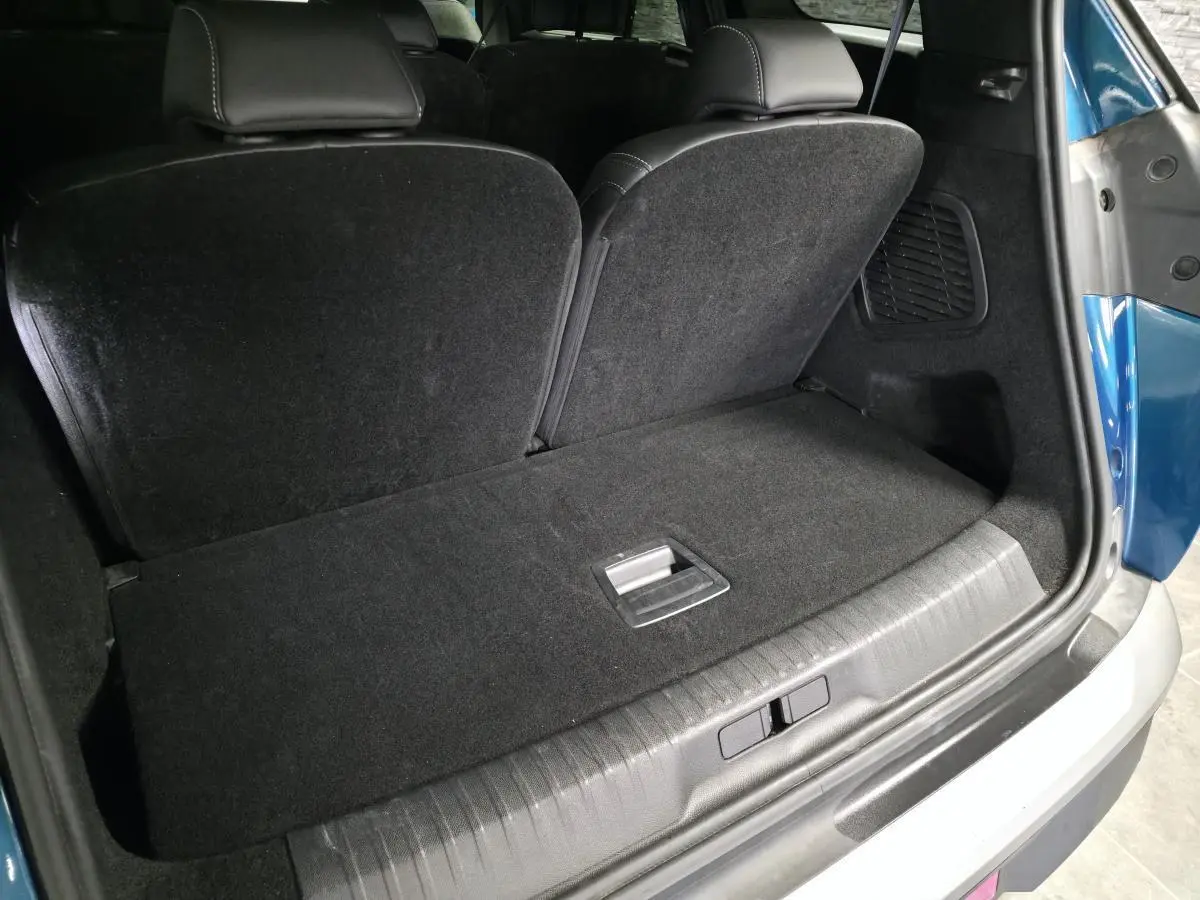 Coffre arrière ouvert d’un Peugeot 5008 bleu, montrant la banquette rabattable et le revêtement noir du coffre.