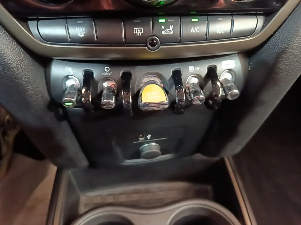 Gros plan sur les commandes centrales avec bouton start/stop jaune dans l’habitacle du MINI Countryman gris clair.