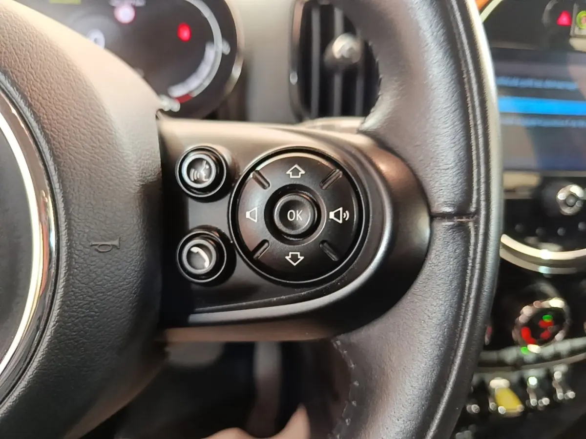 Gros plan sur les commandes multifonctions du volant cuir noir d’un MINI Countryman gris clair, tableau de bord en arrière-plan.