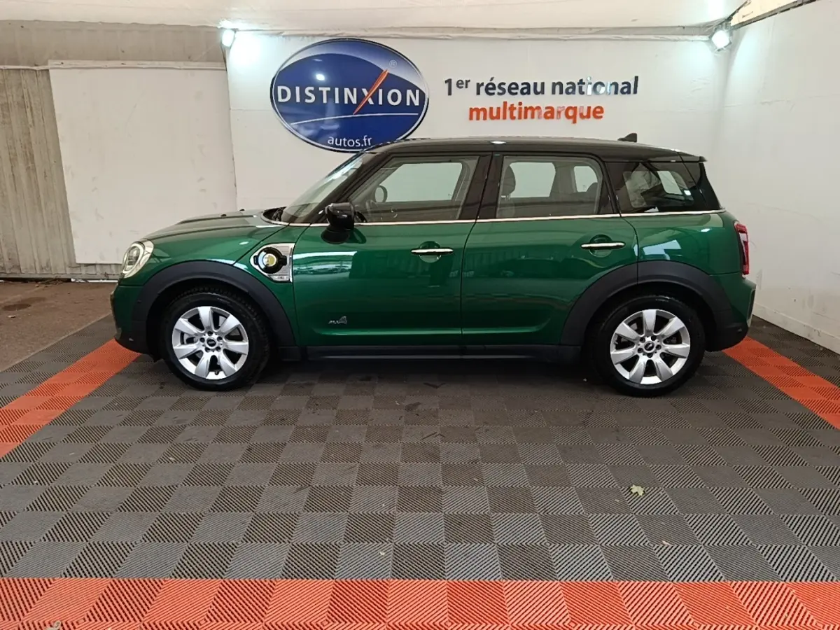 Vue de profil côté gauche d'une MINI Countryman Cooper SE hybride rechargeable vert foncé avec toit noir en intérieur showroom.
