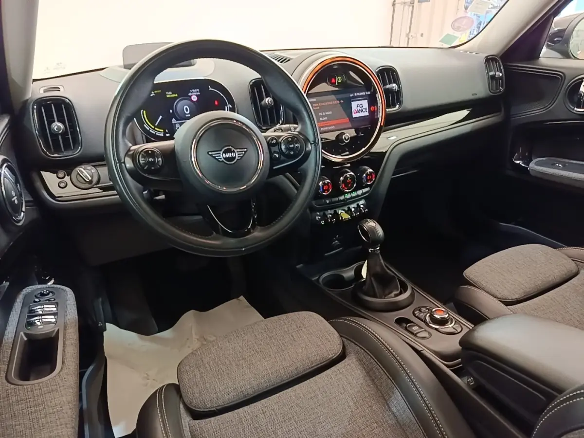 Vue intérieure avant du MINI Countryman Cooper SE avec tableau de bord numérique et sièges tissu gris clair.