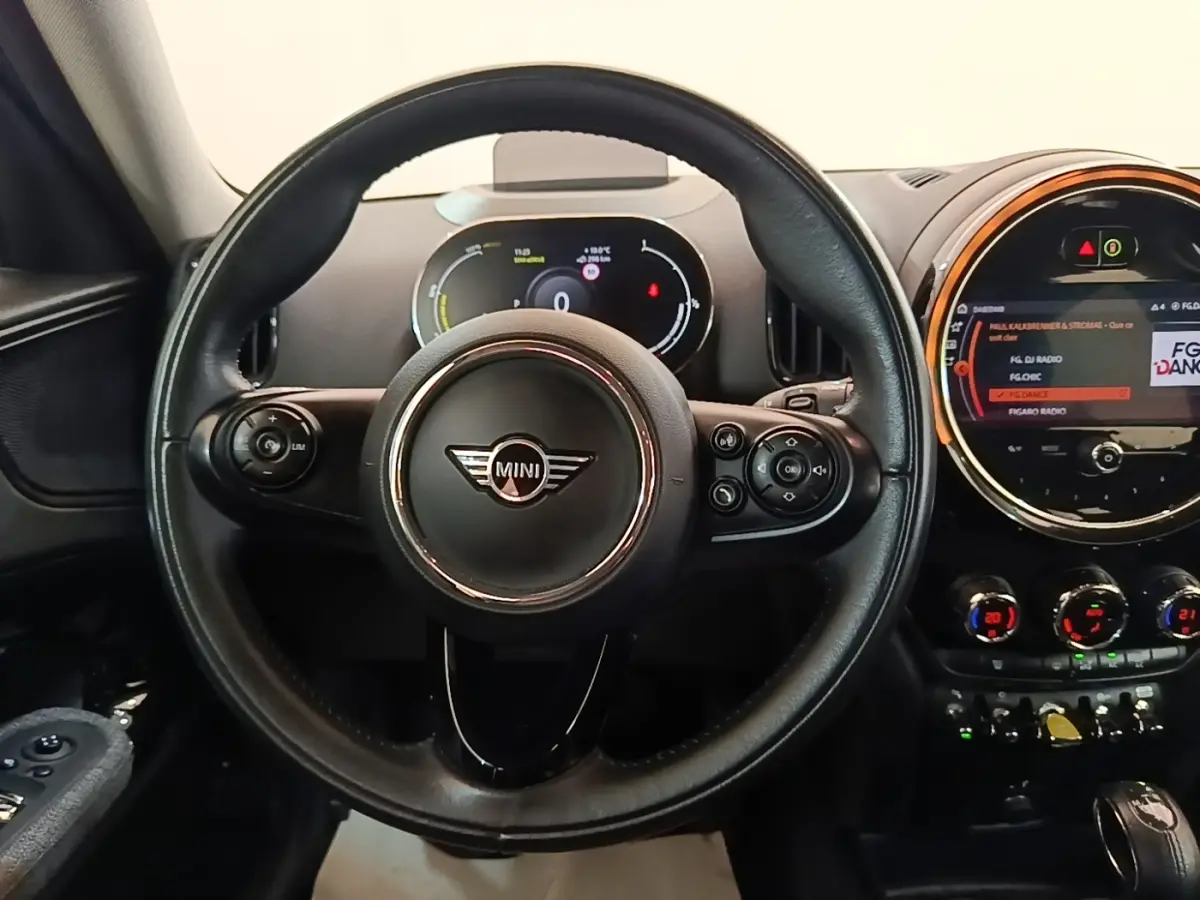 Vue intérieure centrée sur le volant cuir noir et le tableau de bord digital du MINI Countryman hybride gris clair.