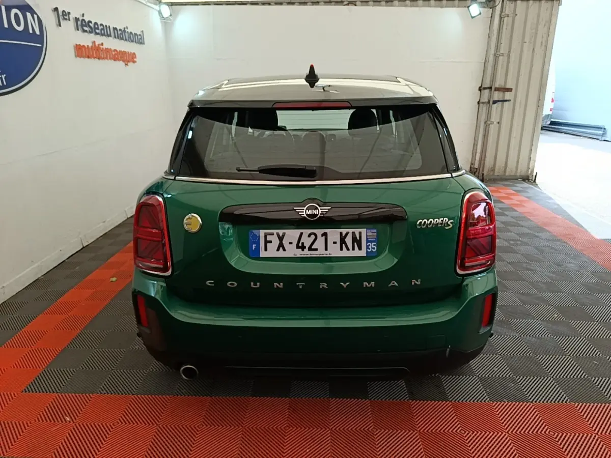 Vue arrière d'une MINI Countryman Cooper S vert foncé avec toit blanc, dans un garage éclairé.