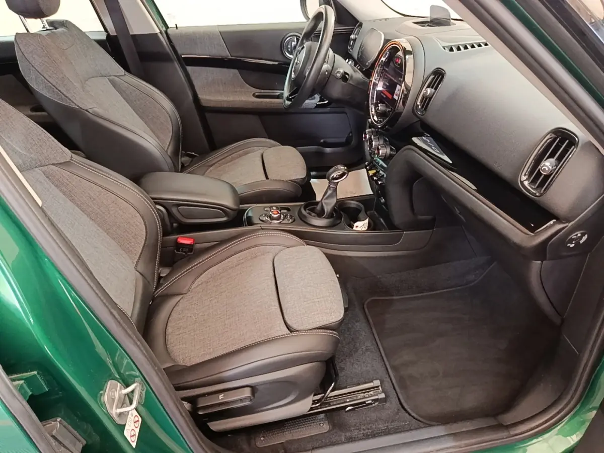Vue intérieure côté conducteur d'une MINI Countryman Cooper SE avec sièges tissu gris et détails noirs, tableau de bord moderne.