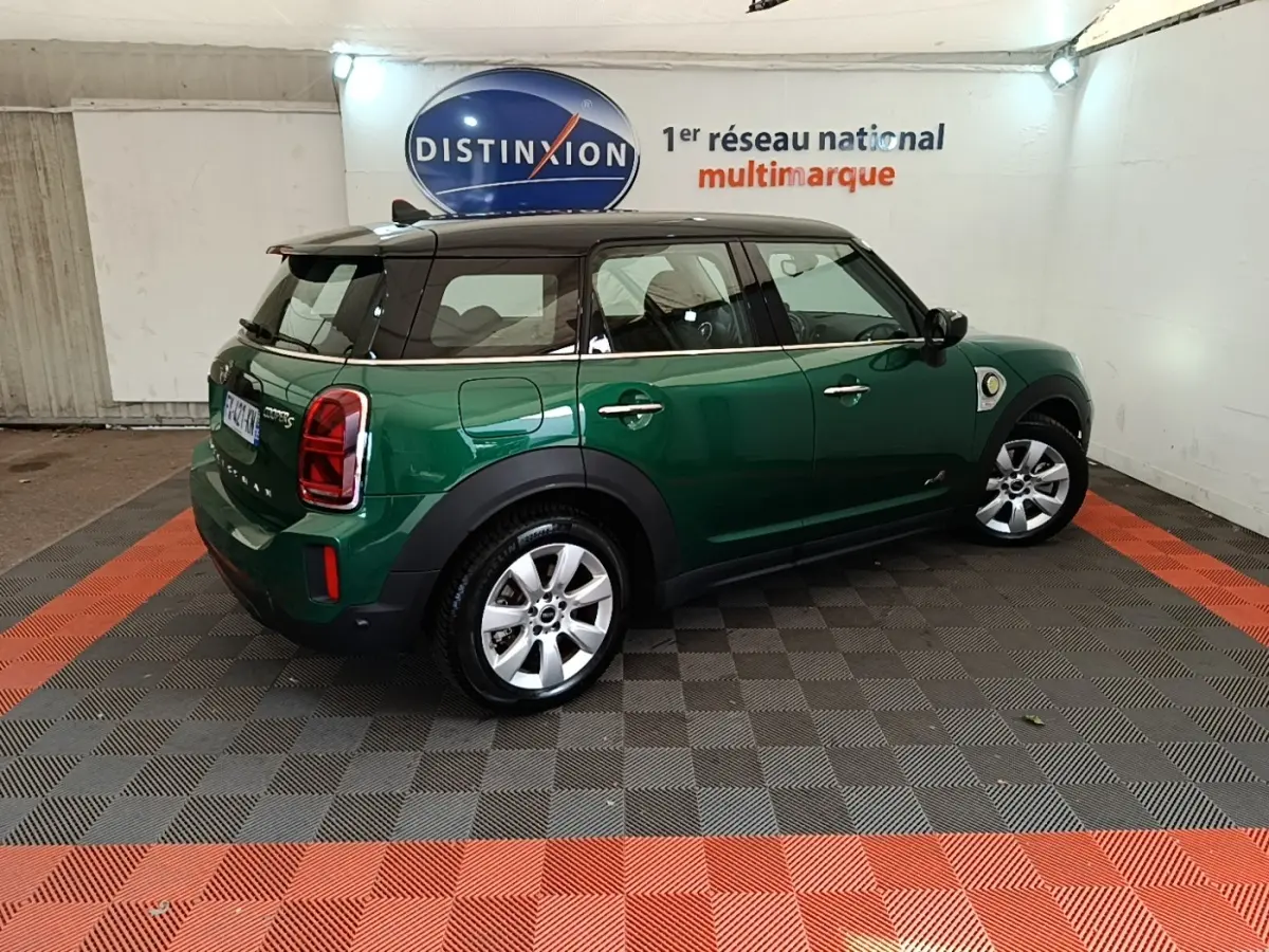 Vue 3/4 arrière droite d'un MINI Countryman hybride rechargeable vert foncé avec toit noir dans un showroom.