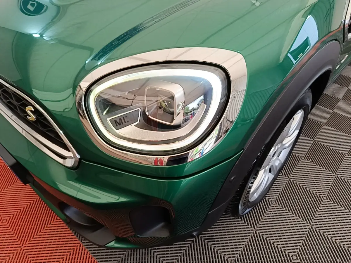 Gros plan sur le phare avant gauche et la roue d’une MINI Countryman verte, soulignant les détails chromés et le logo "S".