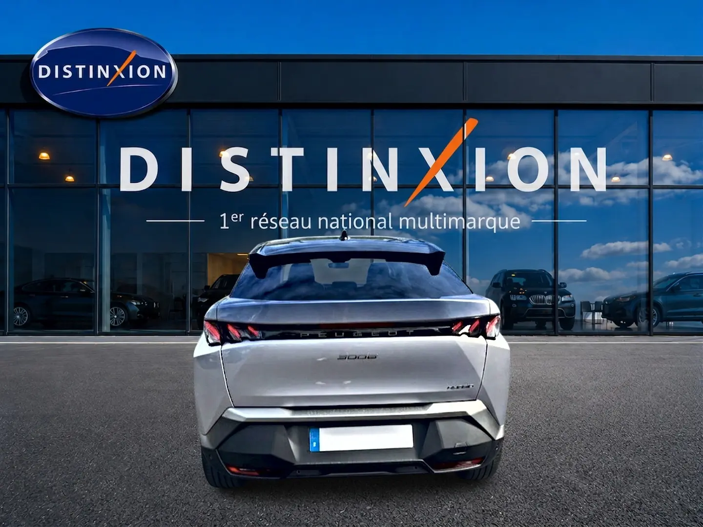 Vue arrière d’un Peugeot 3008 gris Artense 2025, avec feux arrière LED et becquet noir, devant un showroom Distinxion.