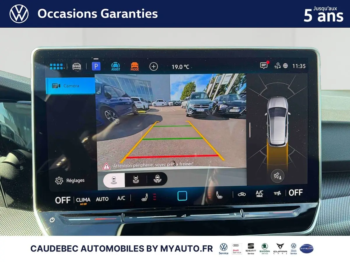 Écran tactile intérieur affichant la caméra de recul et la vue à 360° d'une Volkswagen Golf blanche en stationnement.