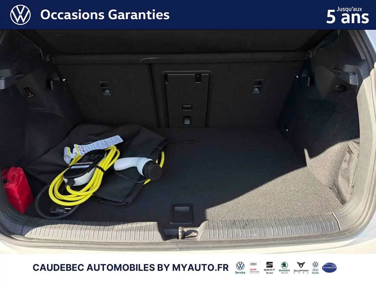 Coffre ouvert d'une Volkswagen Golf blanche 2025 avec câble de recharge électrique visible à l'intérieur.