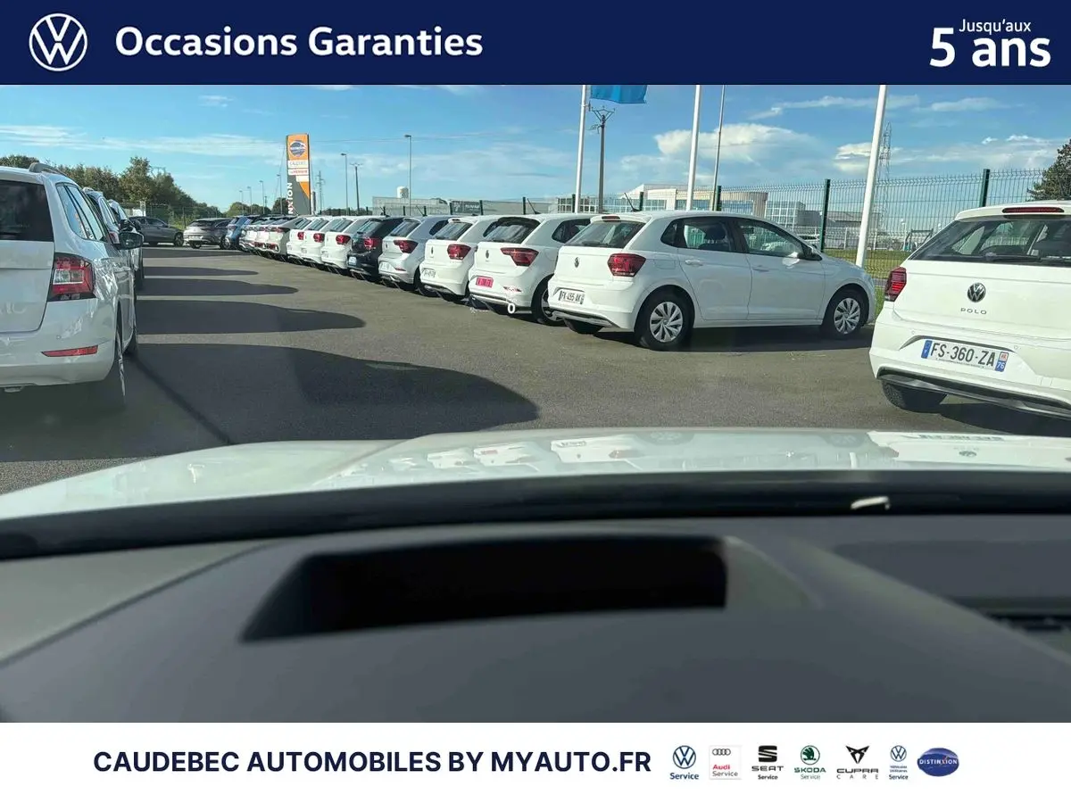 Vue depuis l'intérieur vers l'avant d'une Volkswagen Golf blanche garée de côté droit parmi d'autres véhicules blancs.
