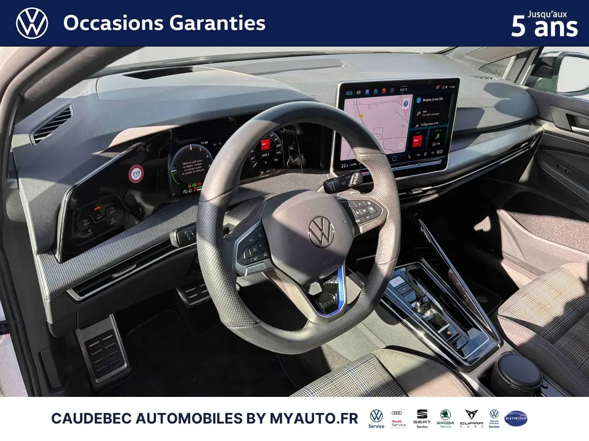 Vue intérieure du poste de conduite de la Volkswagen Golf 1.5 eHybrid 2025, volant cuir multifonction et grand écran tactile central.