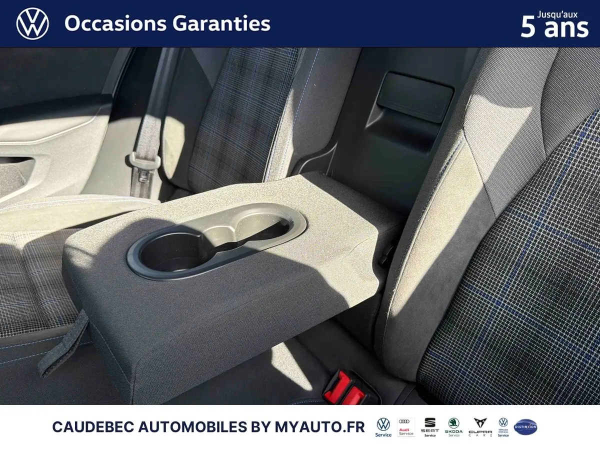 Vue rapprochée de l'accoudoir central arrière avec porte-gobelets sur les sièges tissu gris à motifs bleus de la Volkswagen Golf 1.5 eHybrid blanche.