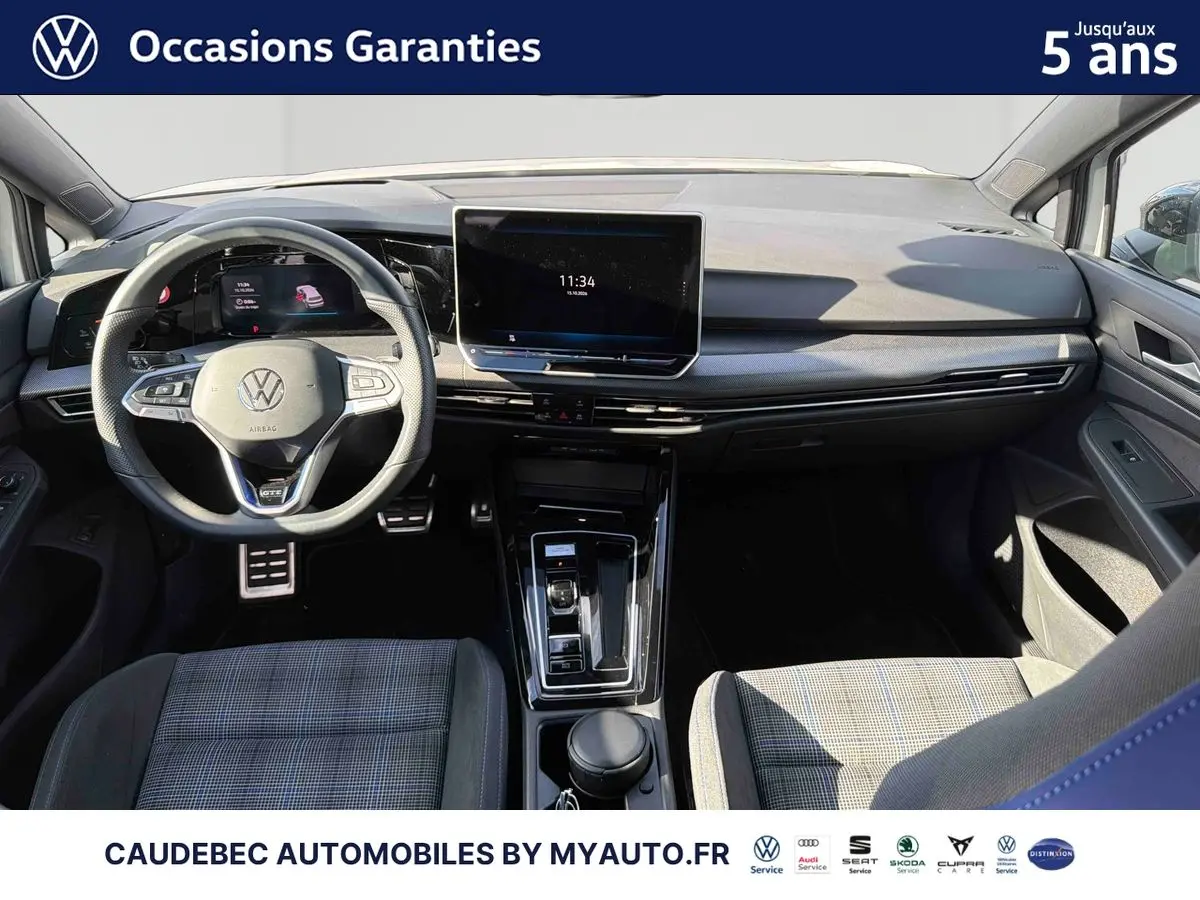 Vue intérieure avant de la Volkswagen Golf 1.5 eHybrid blanche, avec volant multifonction et écran tactile central.
