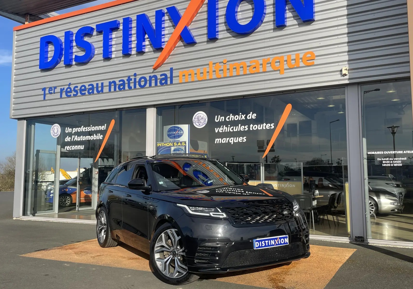 Range Rover Velar noir Santorini en 3/4 avant droit, garé devant une concession Distinxion avec logo visible.