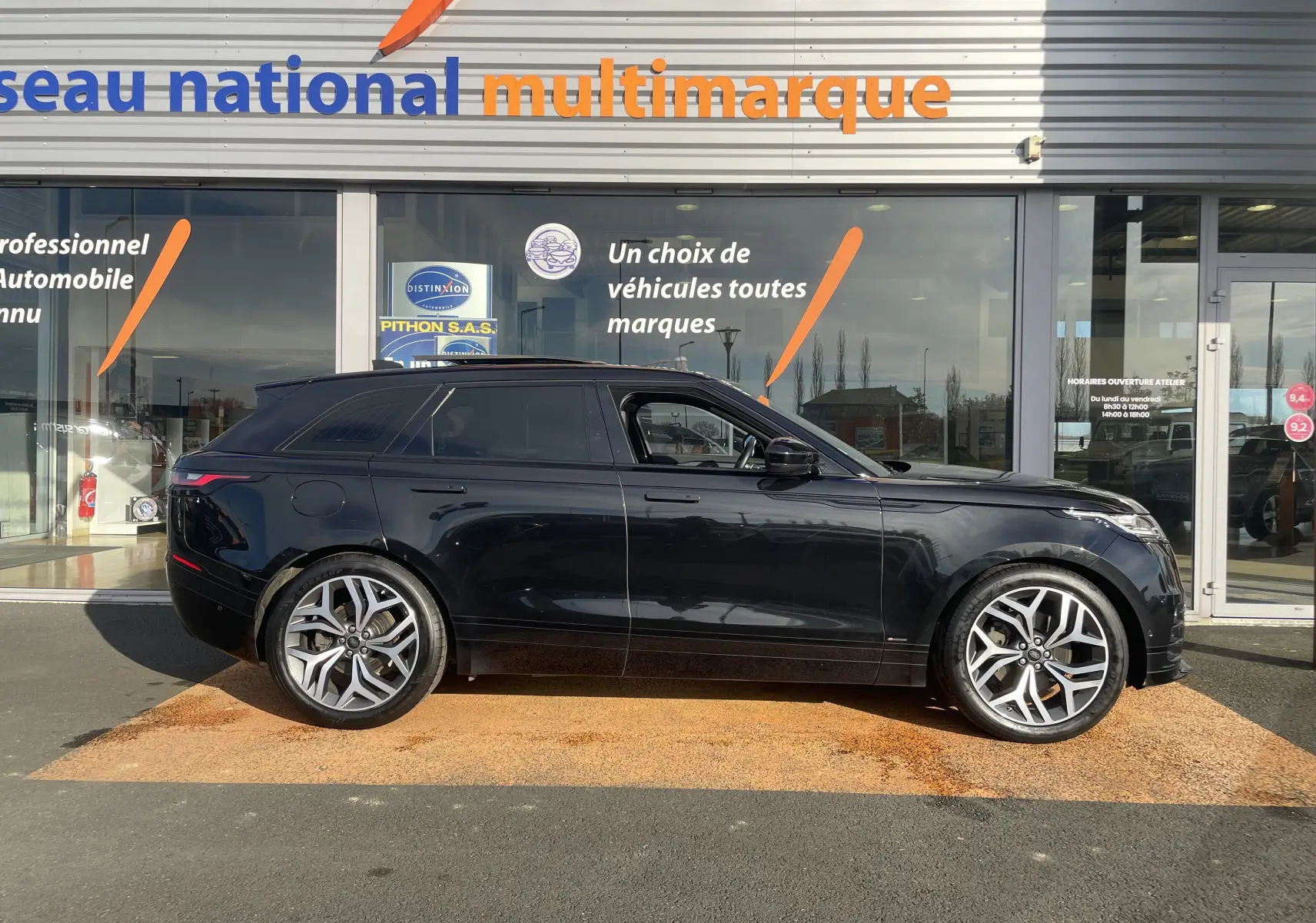 Profil latéral droit du Range Rover Velar noir Santorini 2019 avec jantes alliage distinctives devant un showroom multimarque.