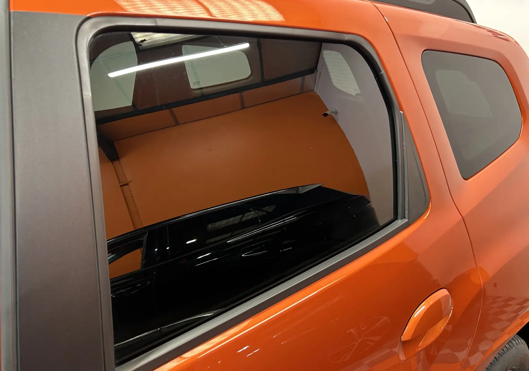 Vue latérale arrière droite du Dacia Duster 2022 orange Arizona avec vitres teintées et poignée de porte intégrée.