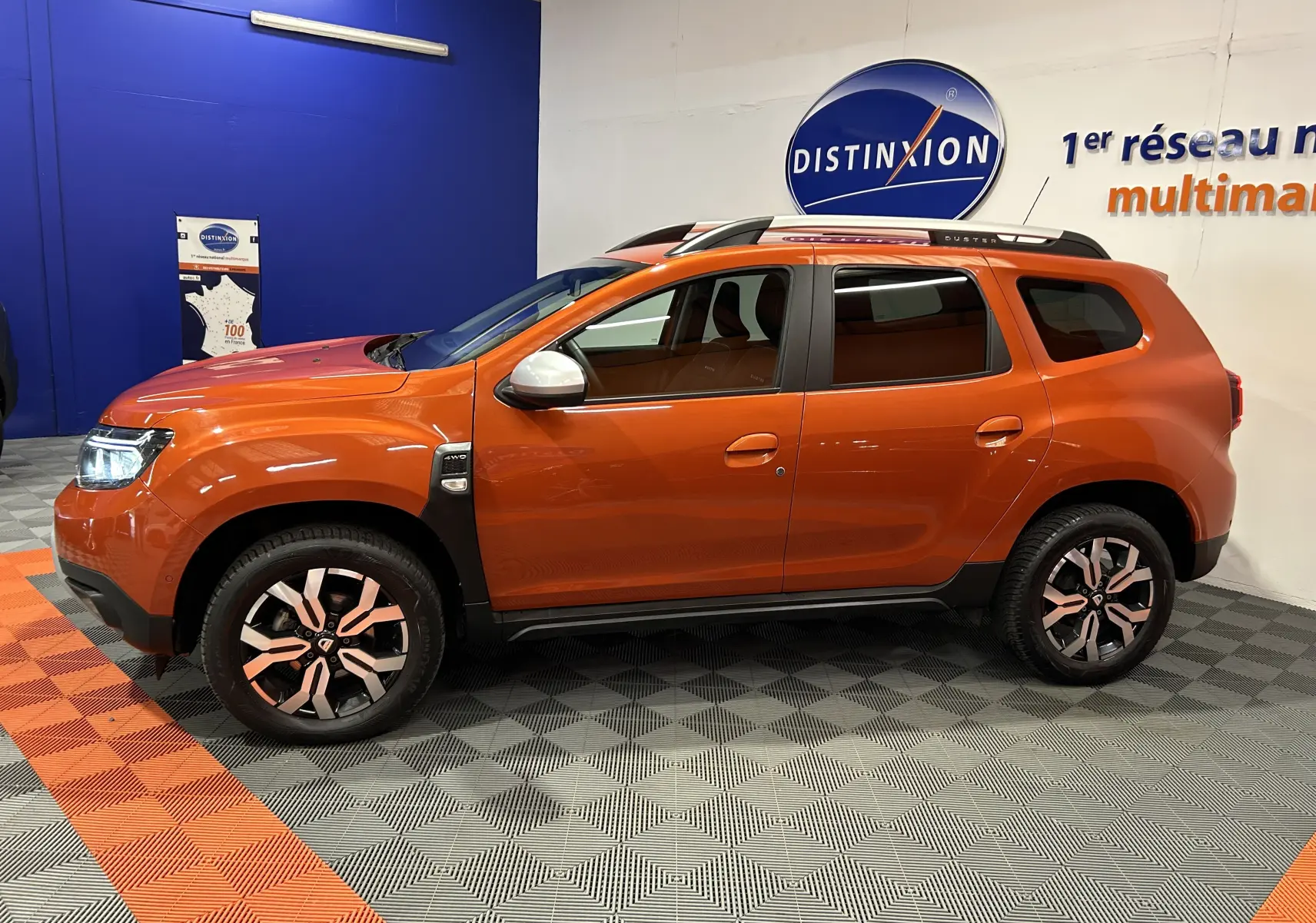 Profil droit du Dacia Duster 2022 orange Arizona avec jantes alliage et barres de toit noires en showroom.