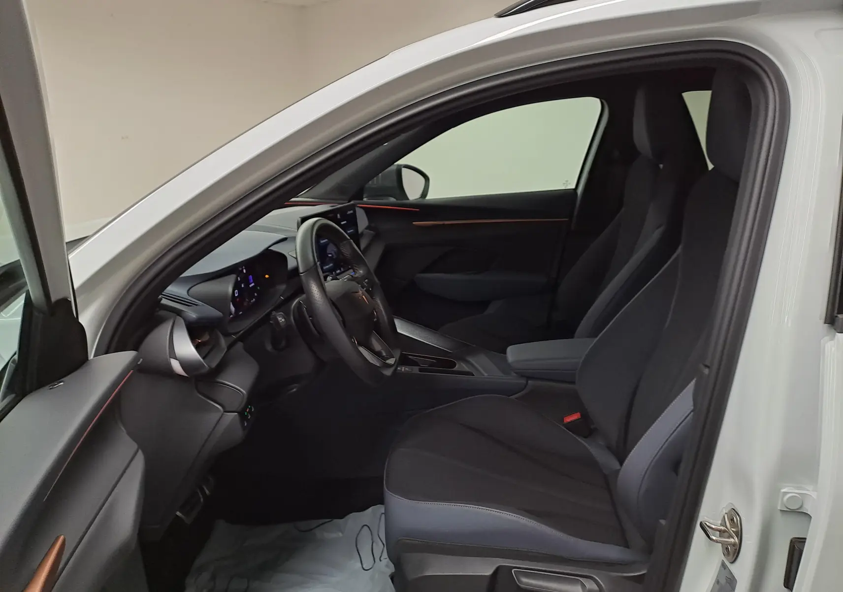 Vue intérieure côté conducteur de la CUPRA TERRAMAR blanc Nevada, avec sièges noirs et tableau de bord moderne.