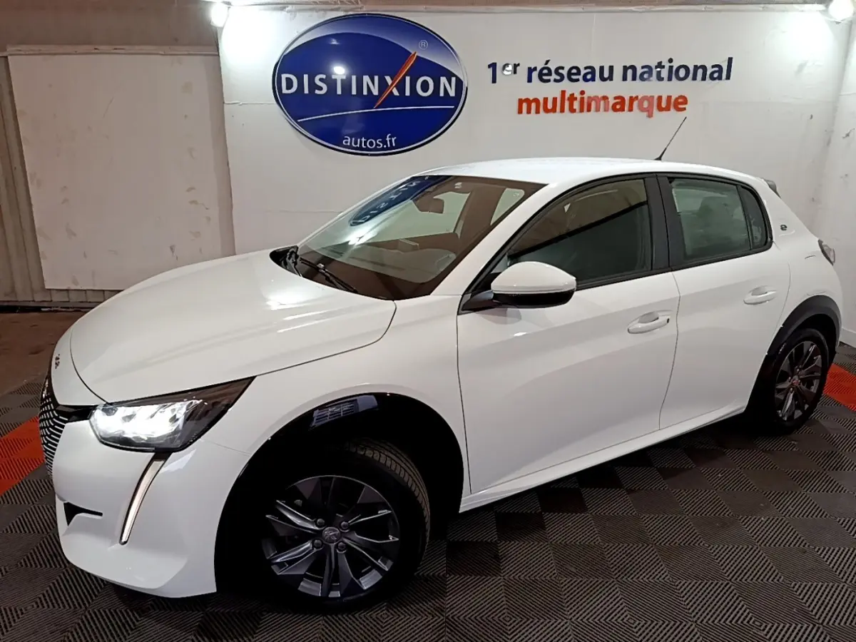 Peugeot 208 électrique blanche vue 3/4 avant droit, avec phares LED allumés et jantes foncées.