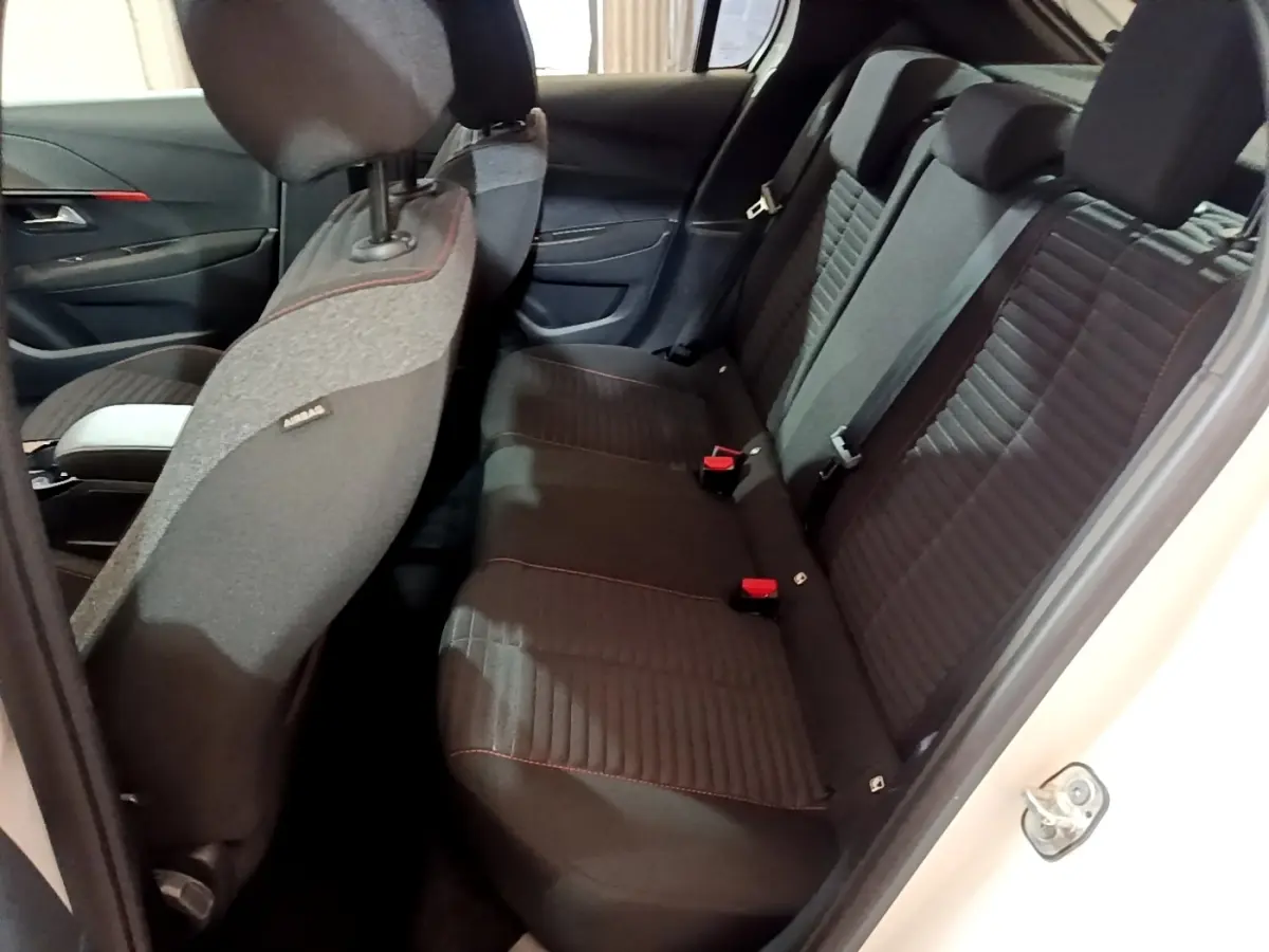 Vue intérieure côté droit sur la banquette arrière noire avec surpiqûres rouges d'une Peugeot 208 Electrique Active Business blanche.