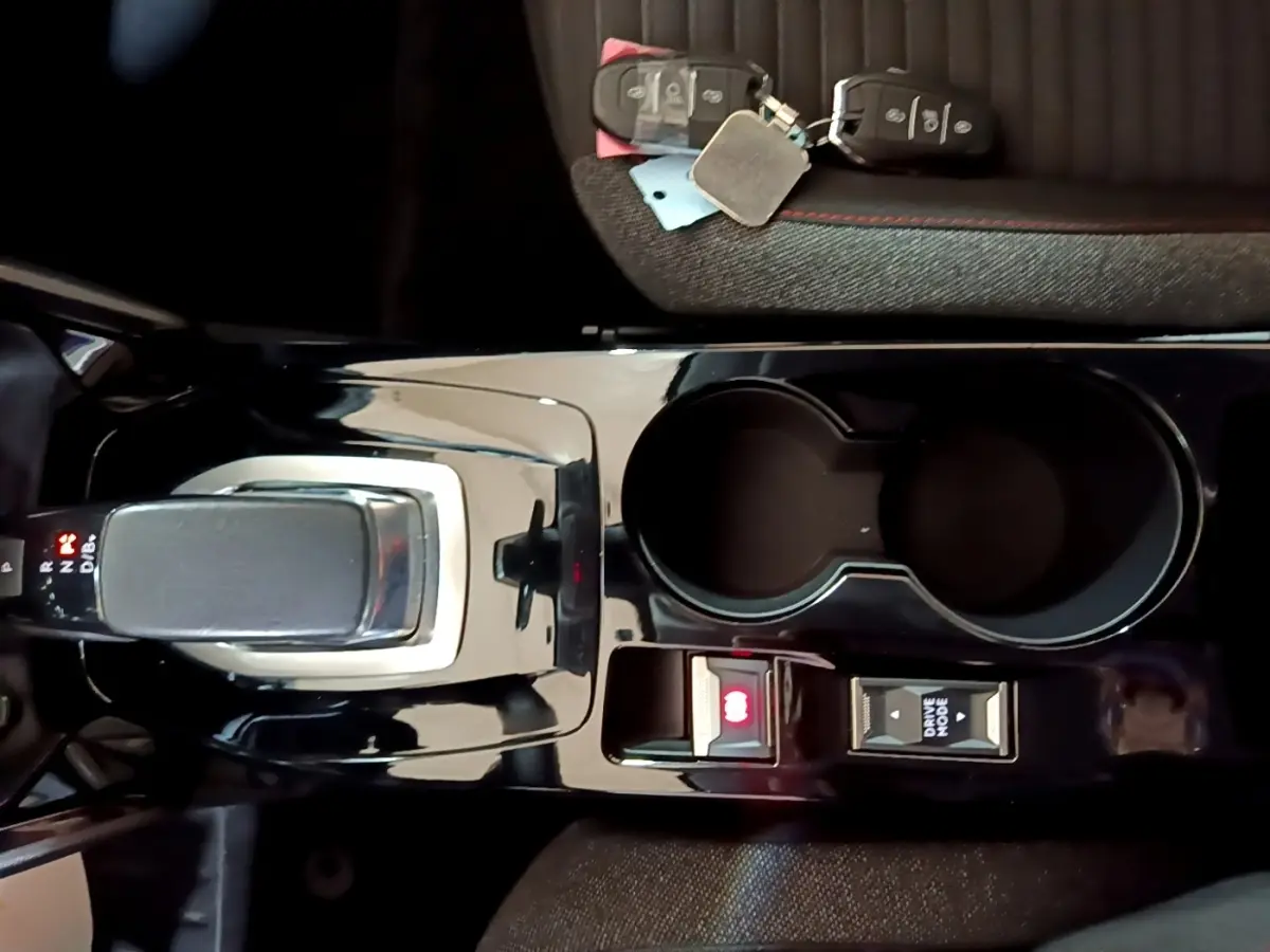 Vue plongeante sur la console centrale noire brillante de la Peugeot 208 électrique avec levier de vitesses et porte-gobelets.